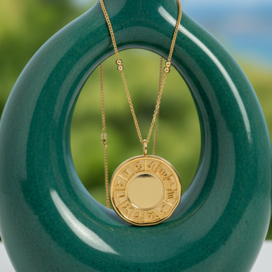 Green vase with a gold necklace hanging through a circular cutout, set against a blurred natural background.