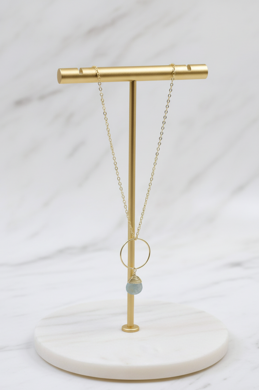 Necklace on a gold stand with a white marble base against a light gray background