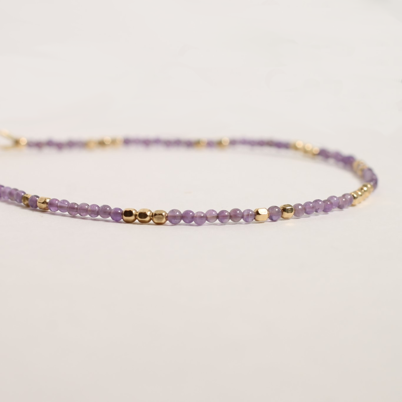 Purple beaded bracelet with gold accents on a light gray background