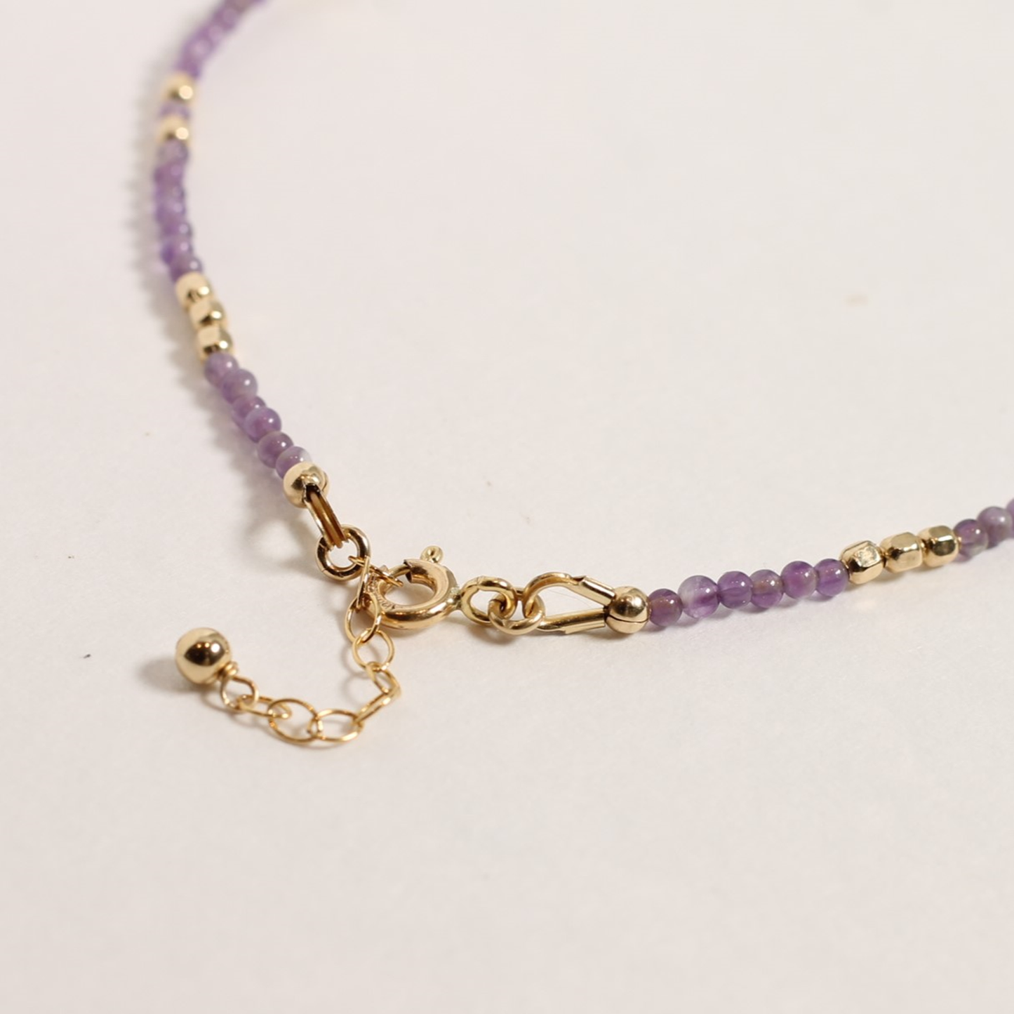Purple beaded bracelet with gold clasp on a light background