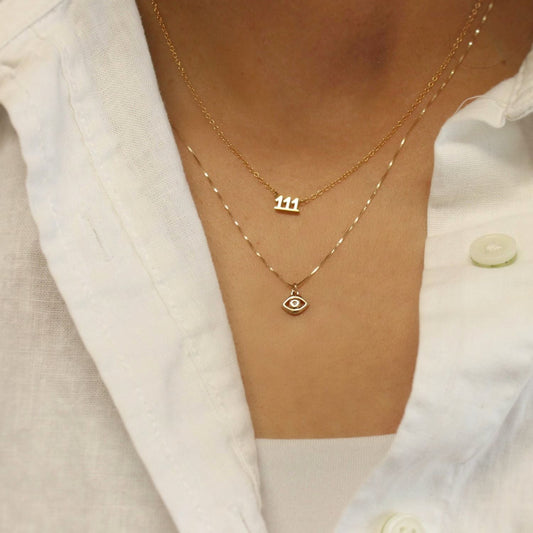 Gold necklaces with number '111' and eye pendant on a white shirt background