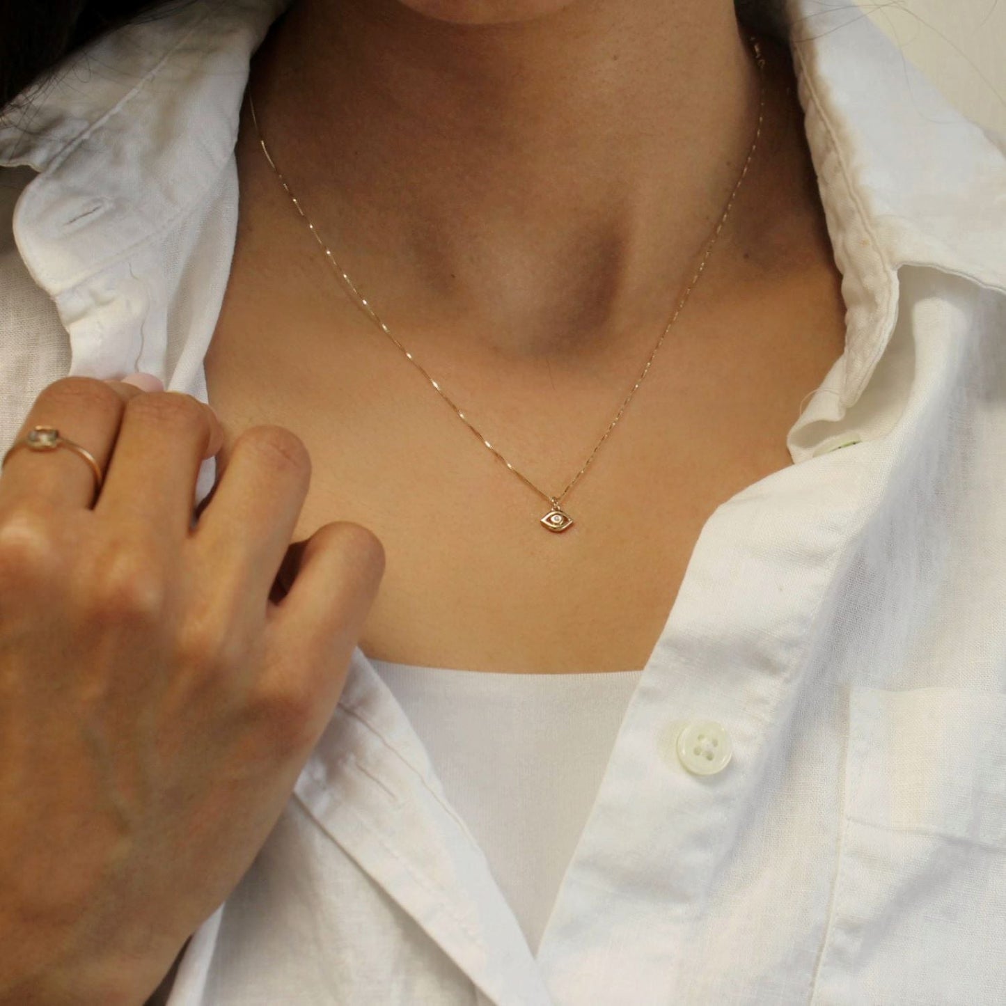 Person wearing a gold necklace with an eye pendant on a white shirt.