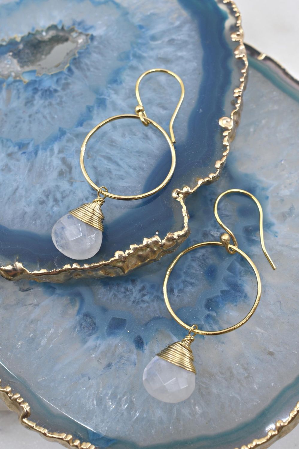 Gold hoop earrings with teardrop-shaped stones on a blue geode background