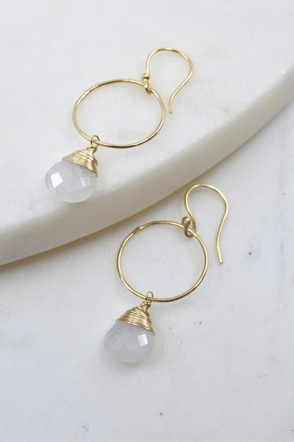 Gold hoop earrings with white teardrop stones on a light background