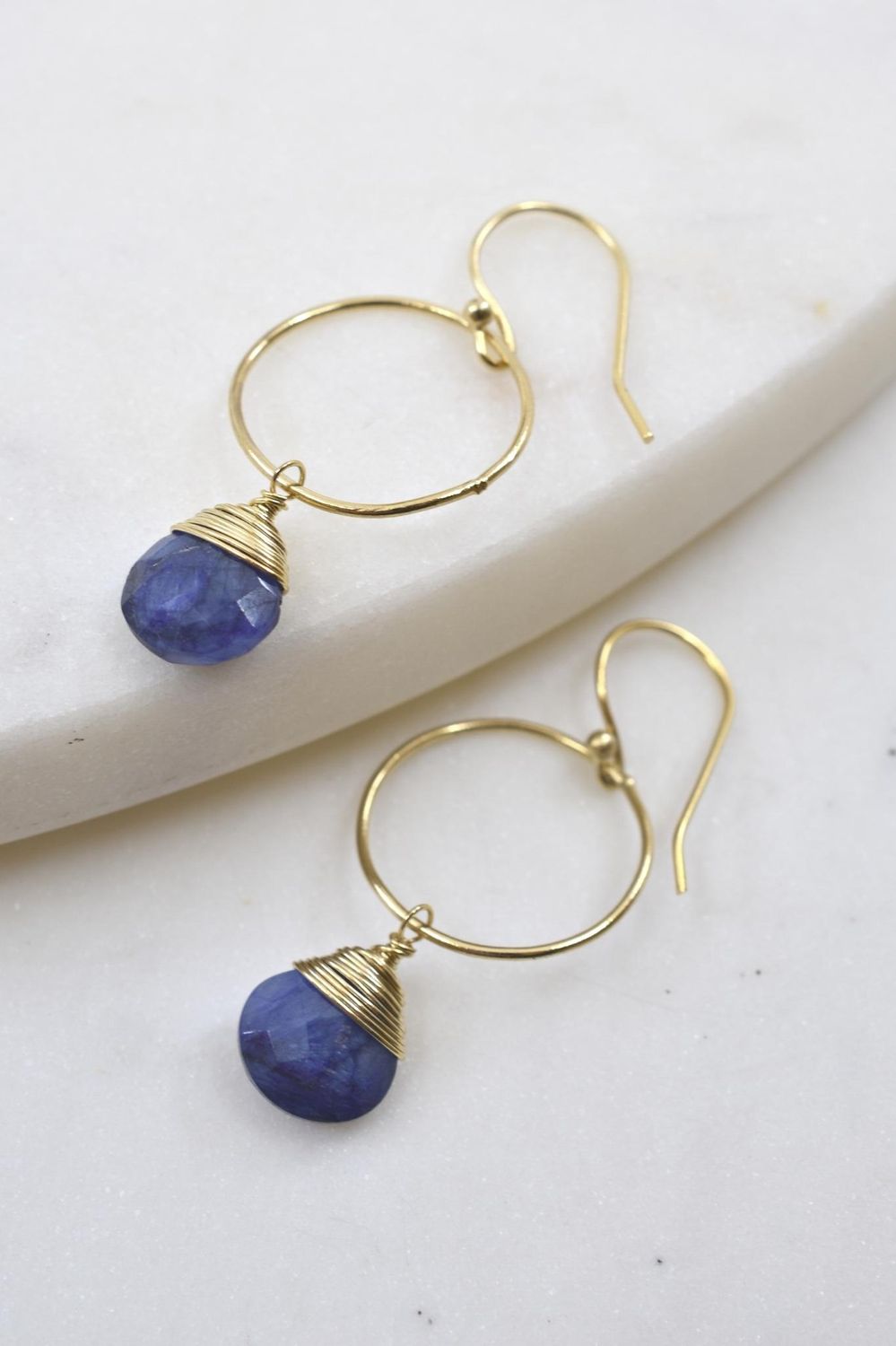 Gold hoop earrings with blue gemstones on a white surface