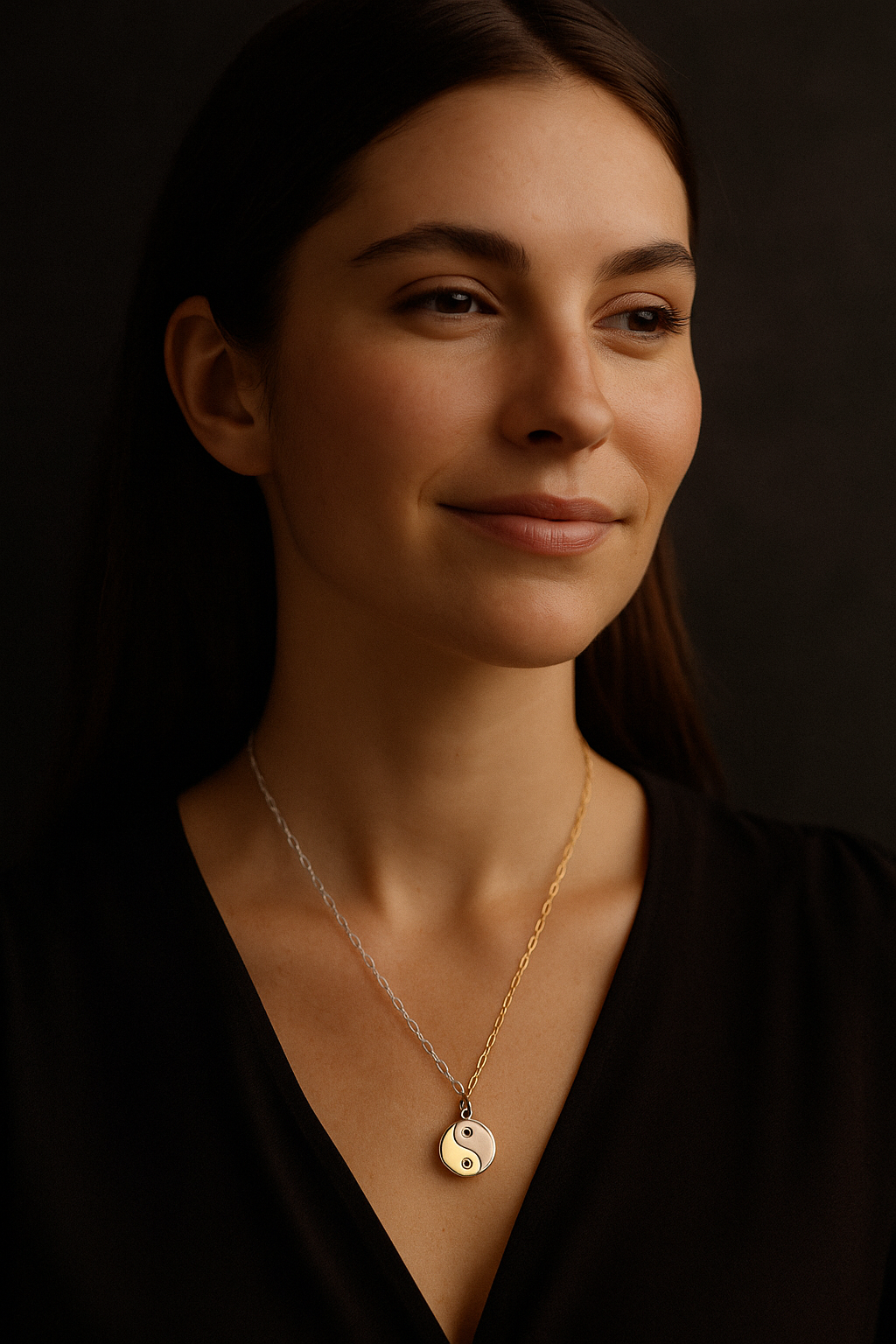 Woman wearing a gold necklace with a yin yang pendant against a dark background