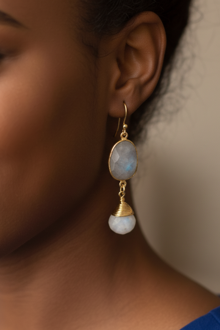 Close-up of a person wearing gold earrings with gemstones against a neutral background