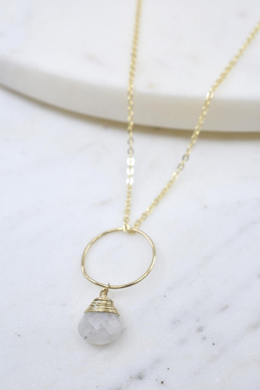 Necklace with gold ring and gray stone pendant on a marble surface
