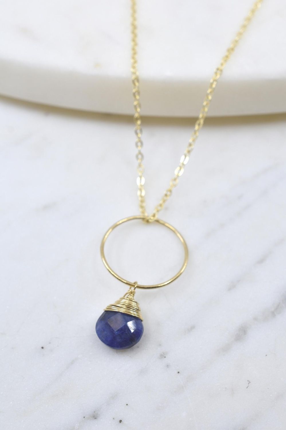 Gold necklace with a blue pendant on a marble surface