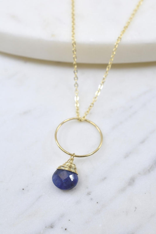 Gold necklace with a blue pendant on a marble surface