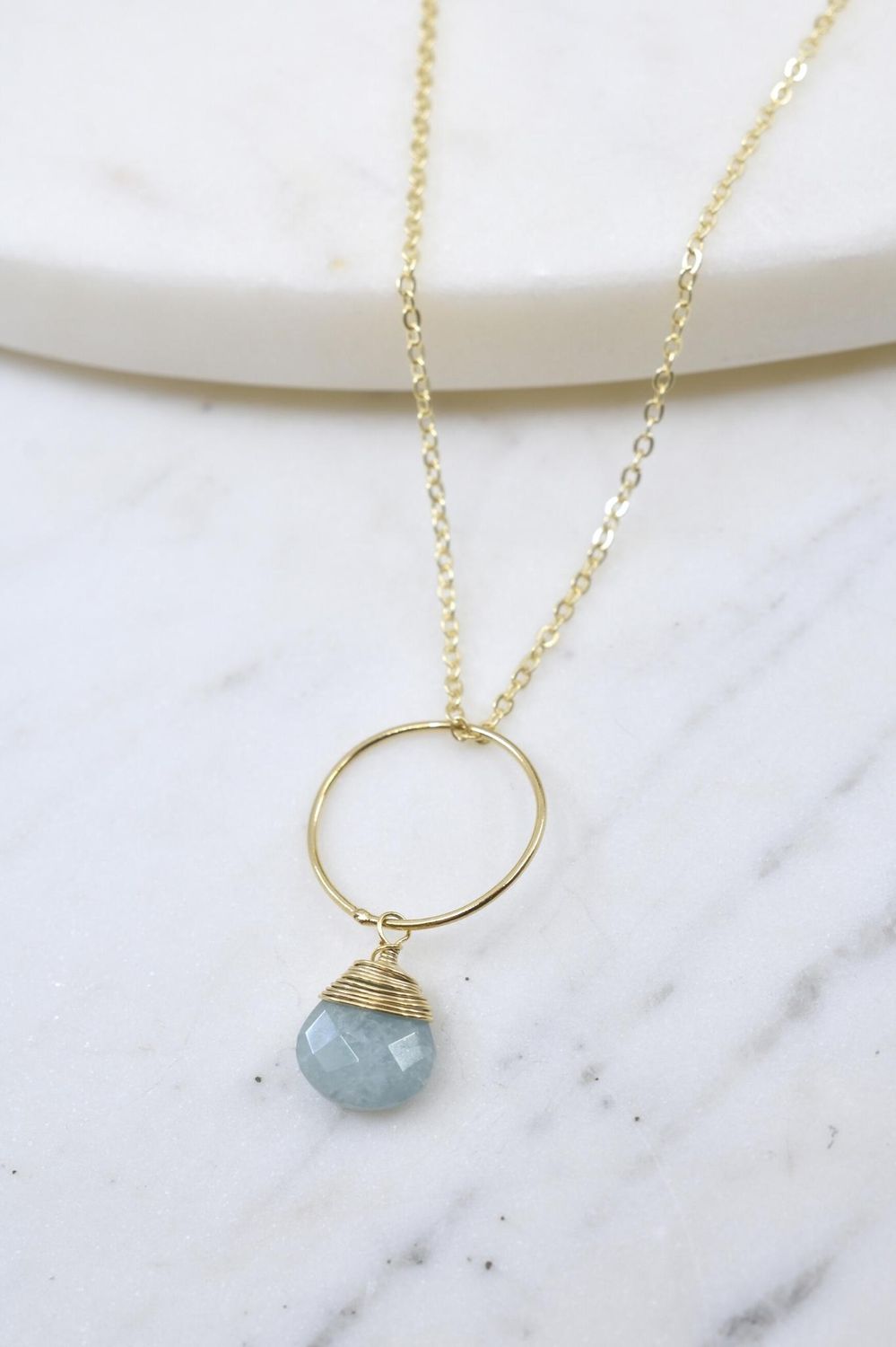 Necklace with a gold ring and blue gemstone pendant on a marble surface