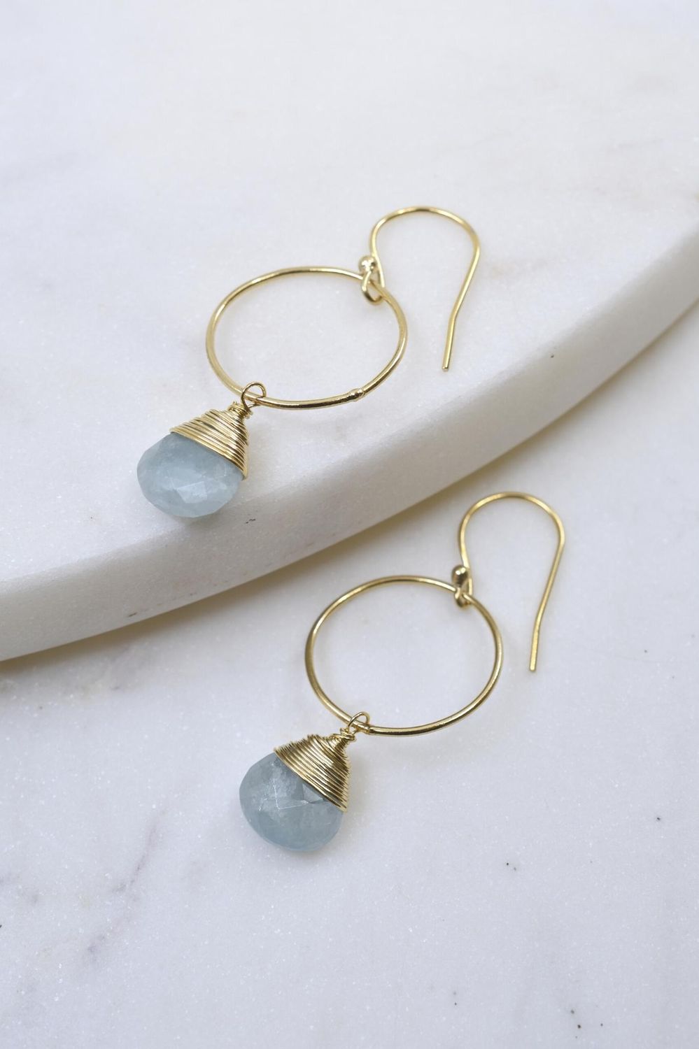 Gold hoop earrings with blue gemstones on a marble surface