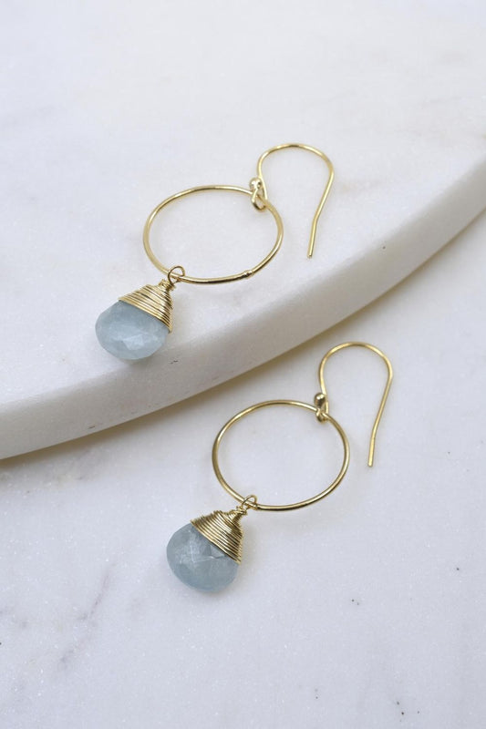 Gold hoop earrings with blue gemstones on a marble surface