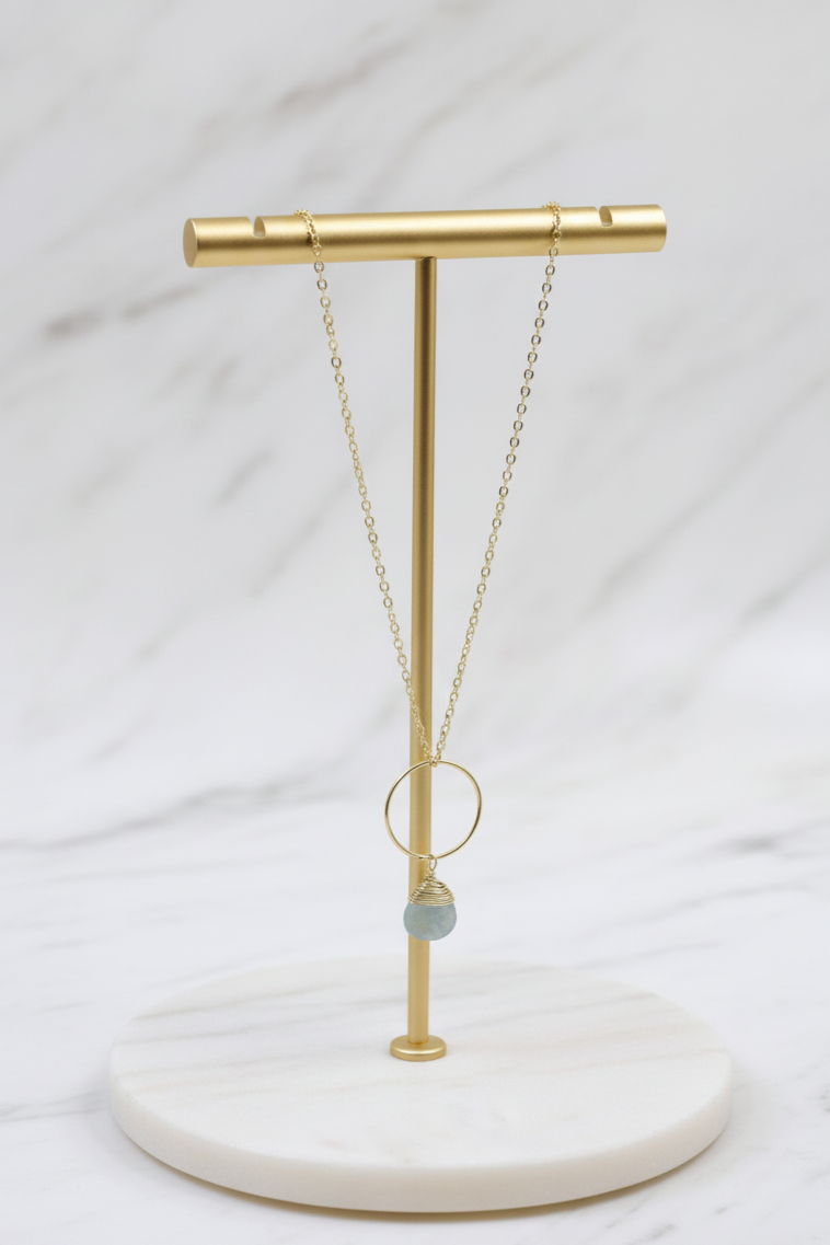 Necklace on a gold stand with a white marble base against a light gray background