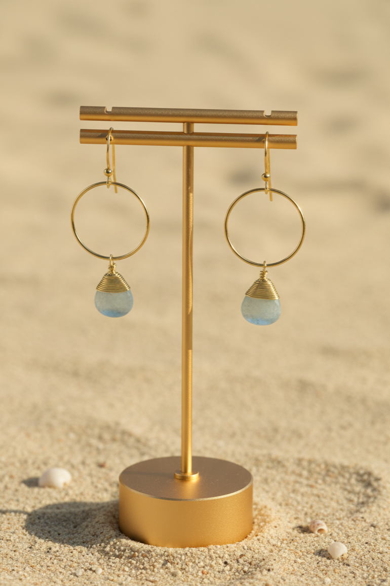 Gold earring stand with hoop earrings on a sandy background