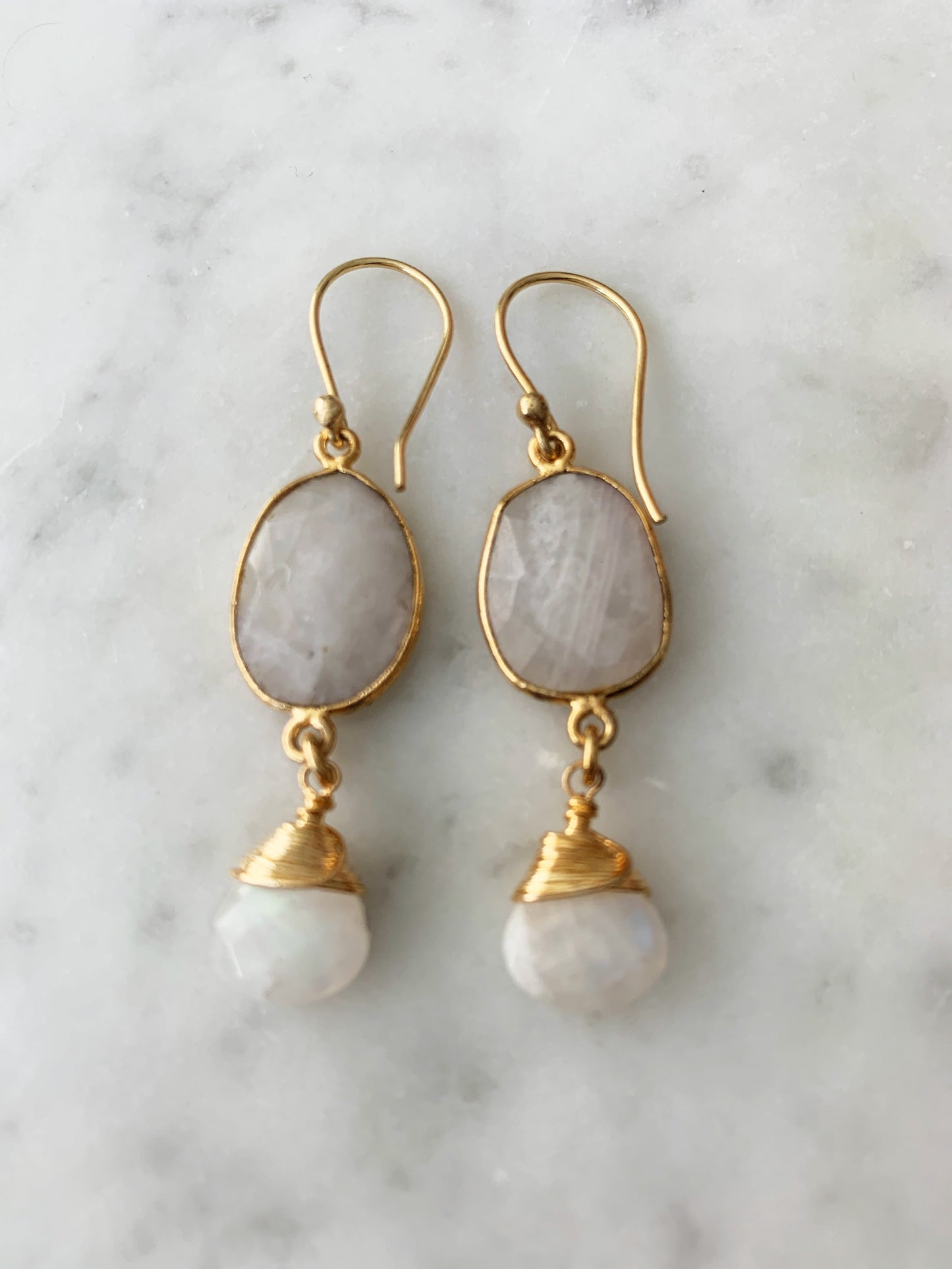 Gold earrings with white stones on a marble background