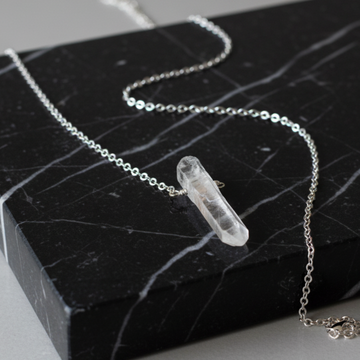 Silver necklace with a clear crystal pendant on a black marble surface