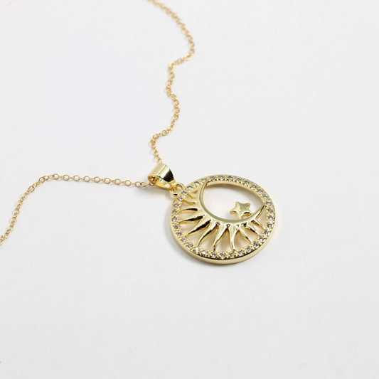 Gold necklace with a circular pendant featuring sun and moon designs on a white background