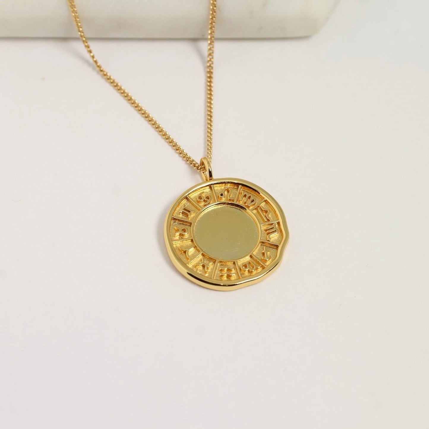 Gold necklace with a round pendant on a white background