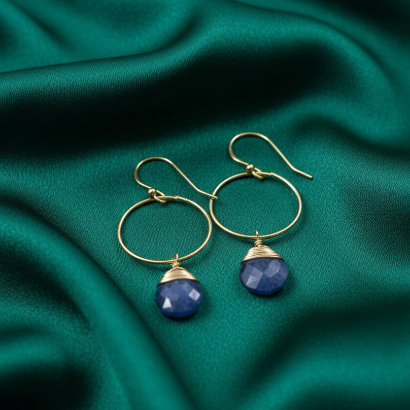 Gold hoop earrings with blue gemstones on a teal fabric background